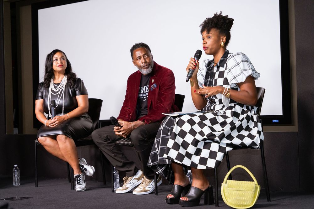 Three panelists at a discussion event, with a woman in checkered dress speaking into a microphone on stage.