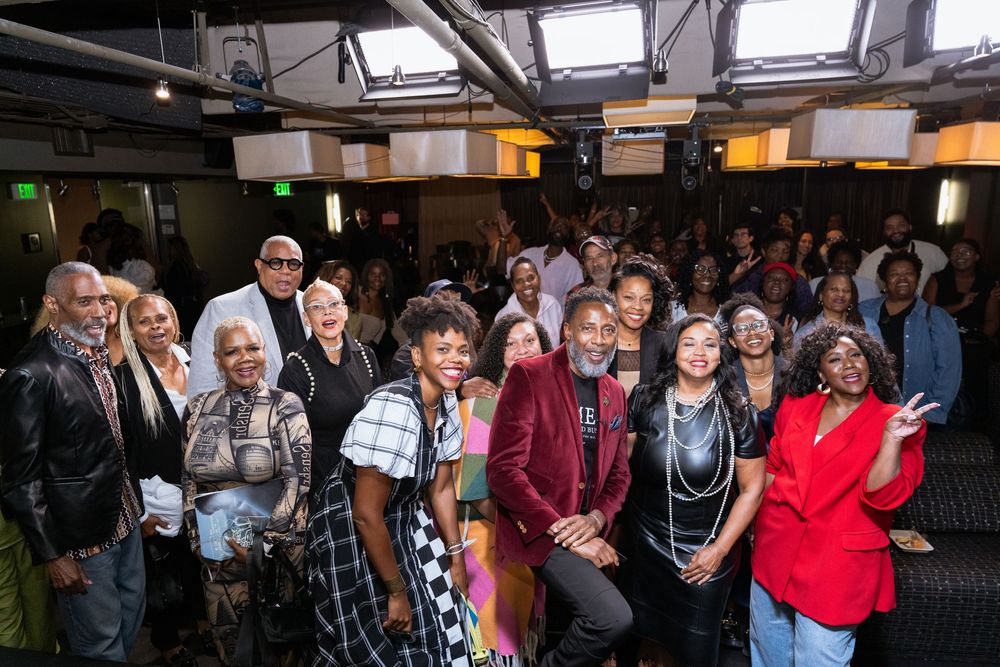 Large diverse group of people posing together at an indoor event venue, smiling for a group photo.