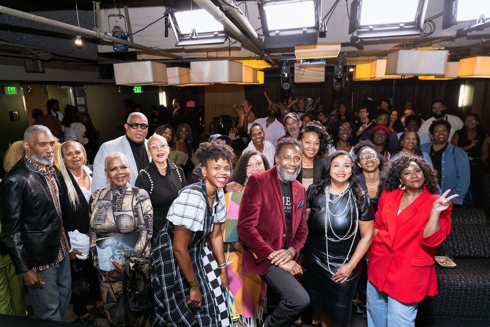 A diverse group of elegantly dressed people posing together at an indoor event with stage lighting.