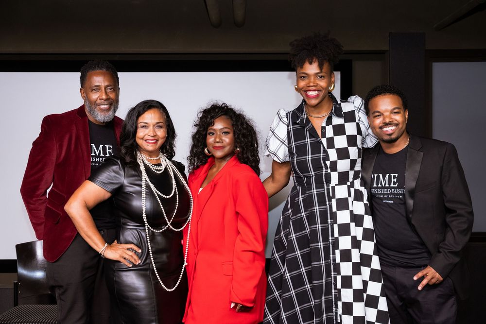 Five people posing together smiling at a formal event, wearing elegant attire including a red suit and checkered dress.