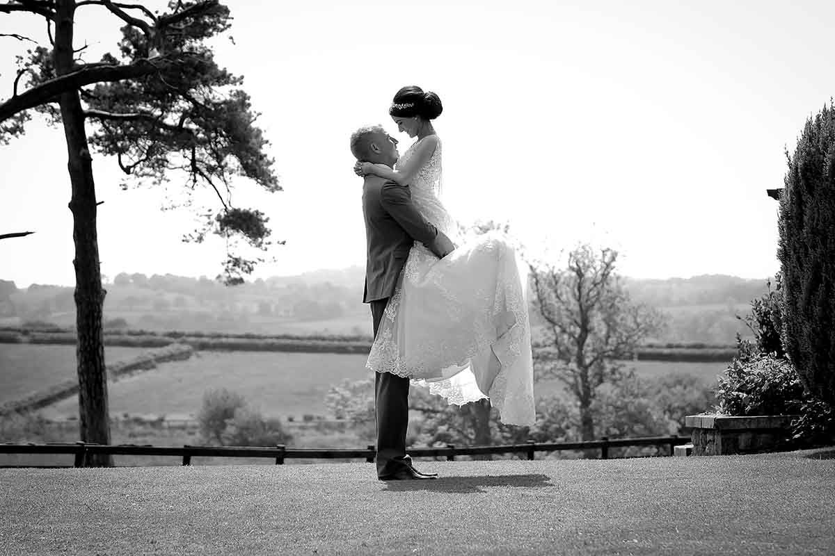 Black and white wedding photo of groom lifting bride on the terrace at Hundith Hill wedding venue Cockermouth