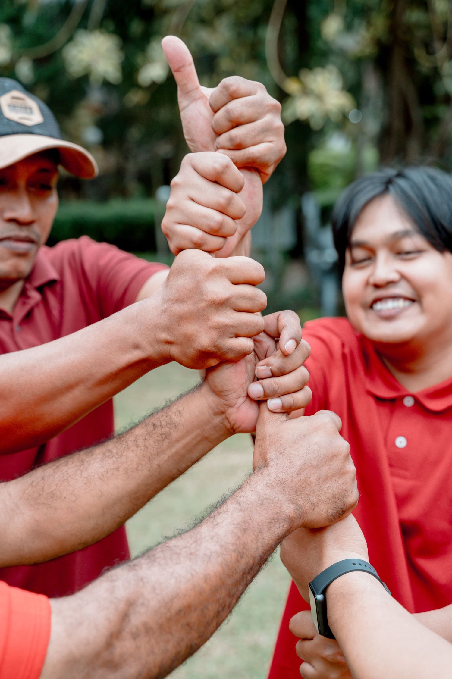 Group of people in red shirts giving thumbs up together outdoors in a team unity gesture.