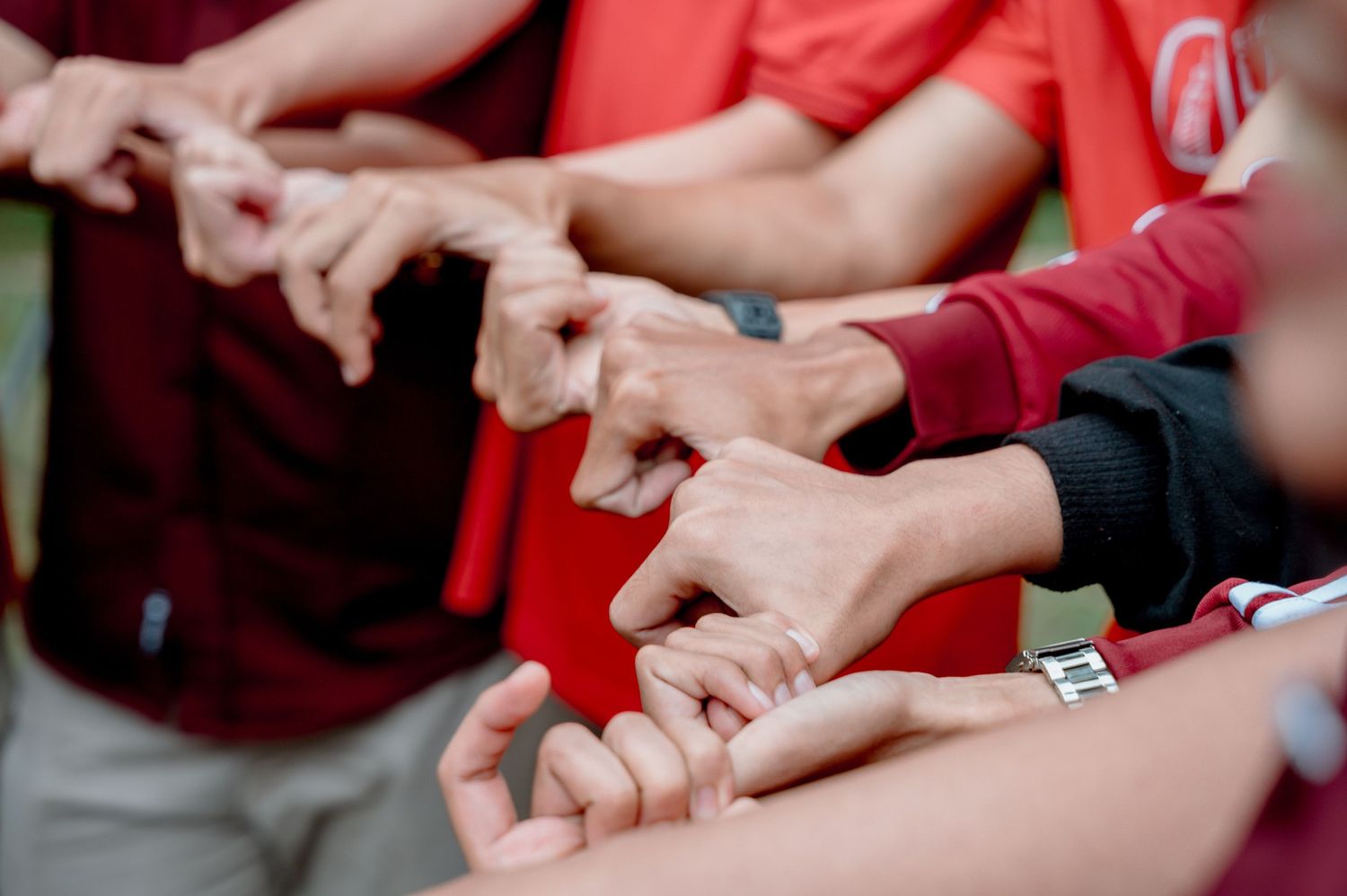 Group of people in red shirts joining hands together in a team huddle outdoors.