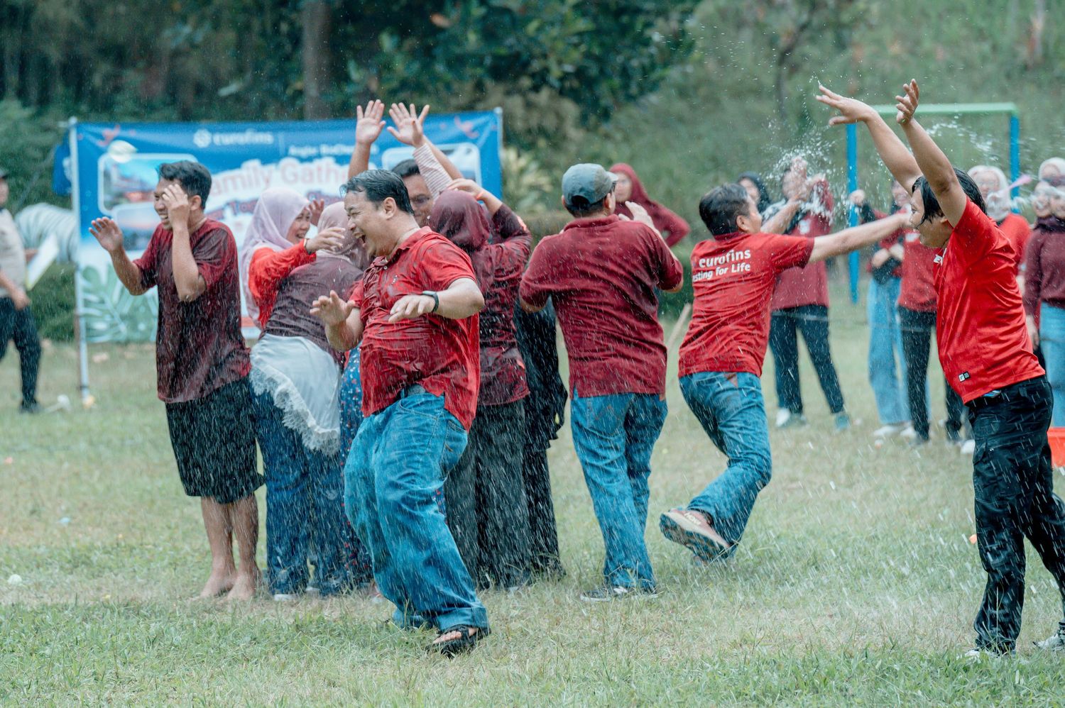 Group of people in red shirts playing outdoor water game activity on green grass field during team building event.
