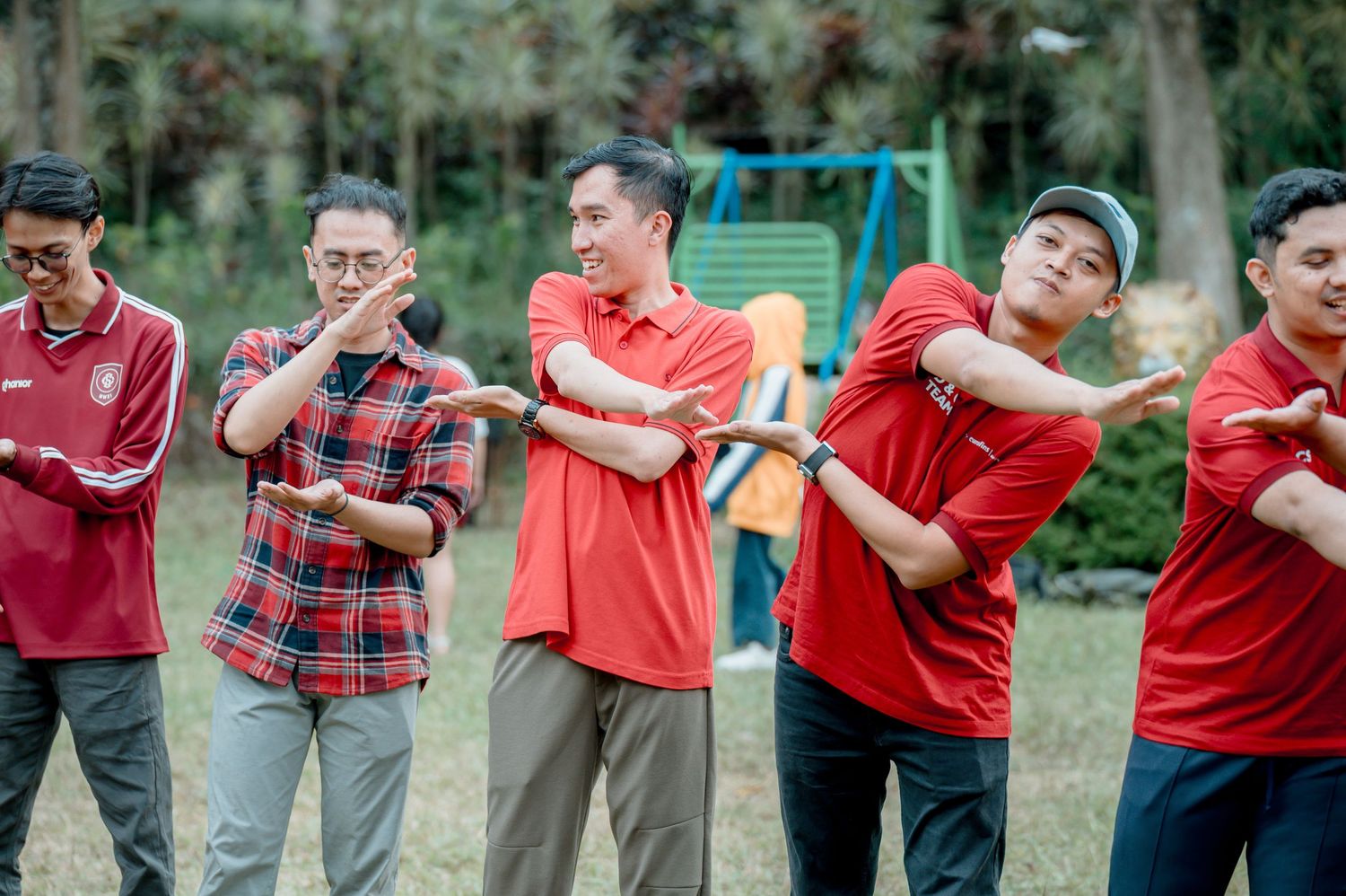Group of men in red shirts doing a fun outdoor team-building activity in a park setting.