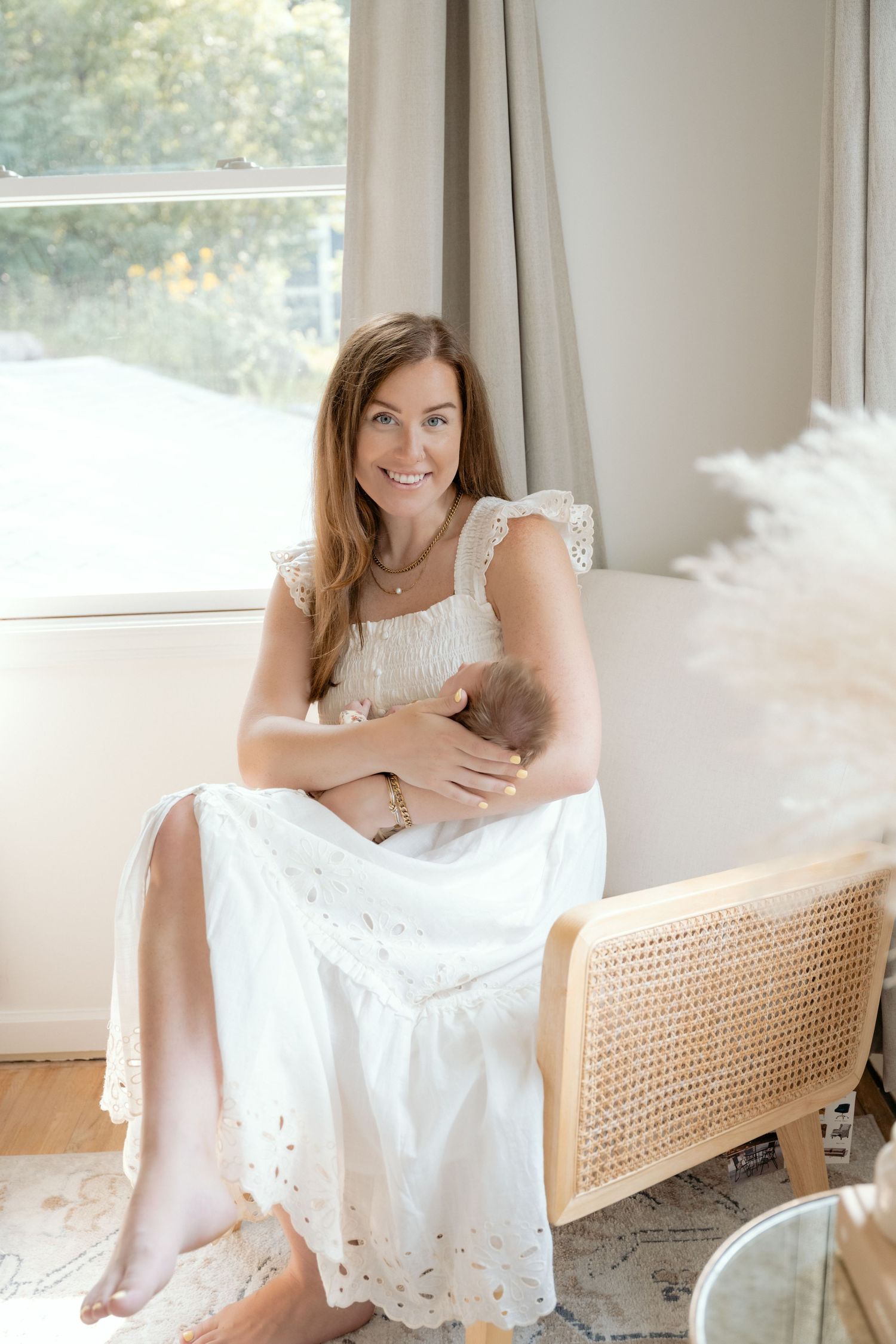 Mom holding newborn baby in a white dress and bright room for clean aesthetic in-home newborn portraits in Minnetonka, MN.