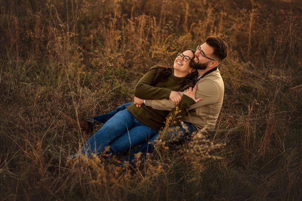 Couple embracing and laughing together in a golden autumn field during a romantic outdoor engagement photo session.
