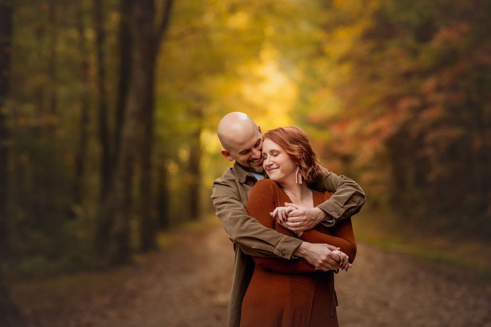 Couple embracing on a forest path surrounded by vibrant autumn foliage in warm orange and yellow tones.