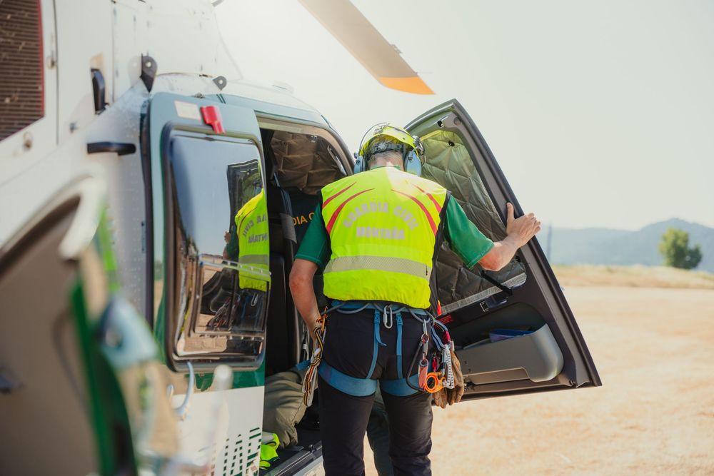 Two rescue workers in high-visibility vests boarding a helicopter during an emergency medical operation outdoors.