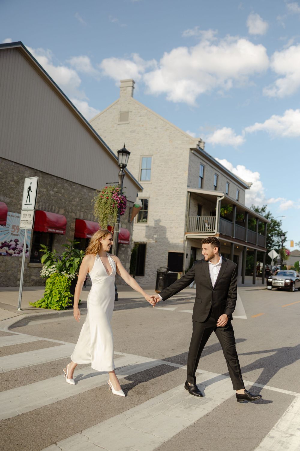 Stylish bride and groom holding hands while crossing a street in a charming small town.