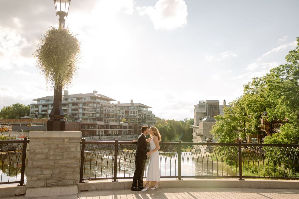 Bride and groom kissing on a waterfront promenade with modern residential buildings behind them.