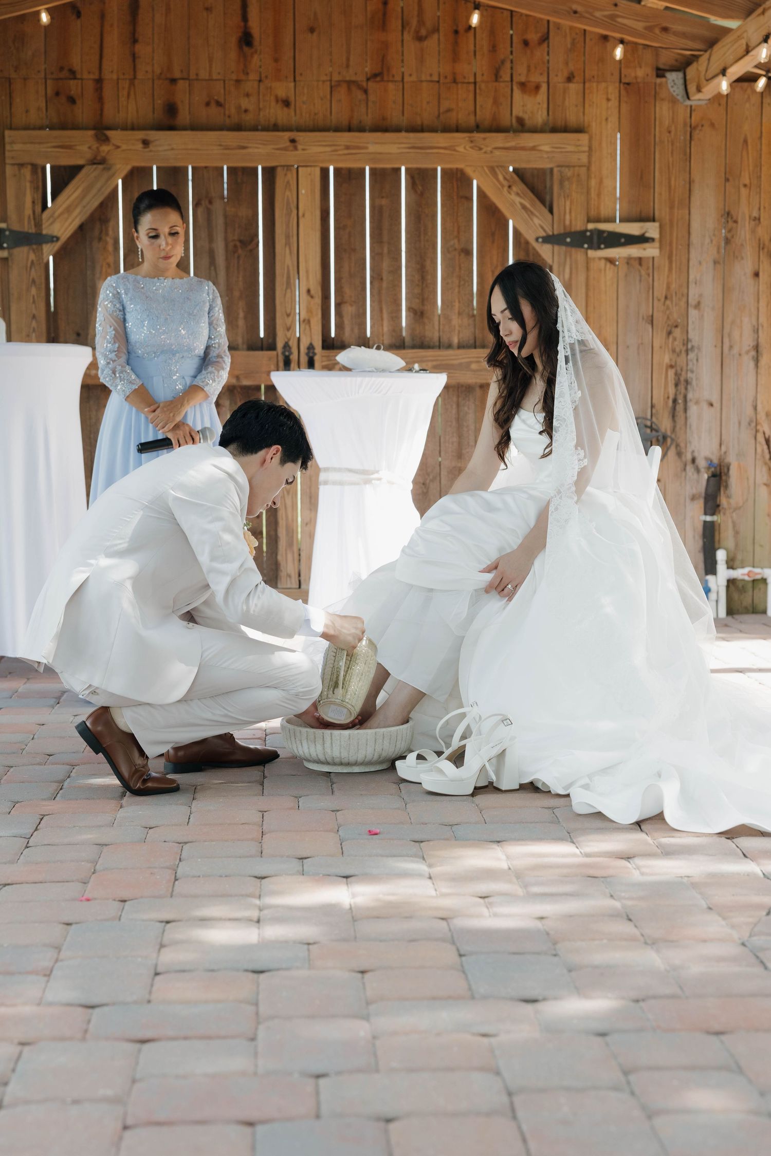 Groom washing bride's feet in a barn during a traditional Christian wedding foot-washing ceremony.