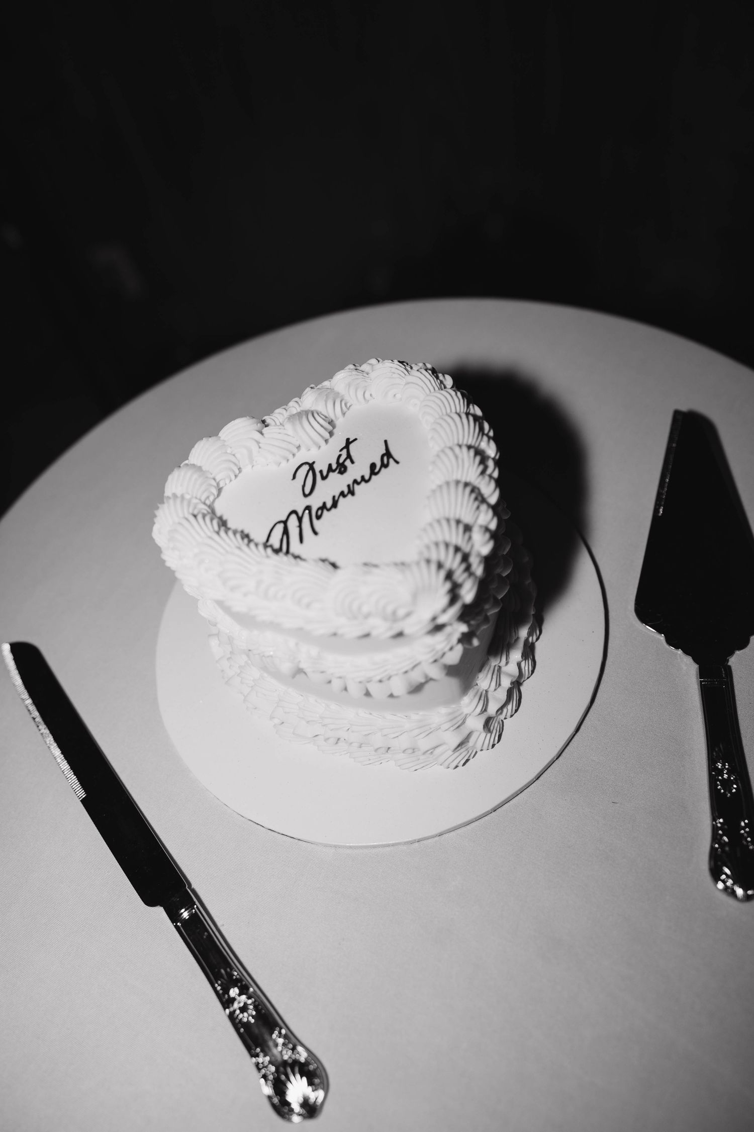 Heart-shaped white wedding cake inscribed with Just Married on a round plate with a knife and server.