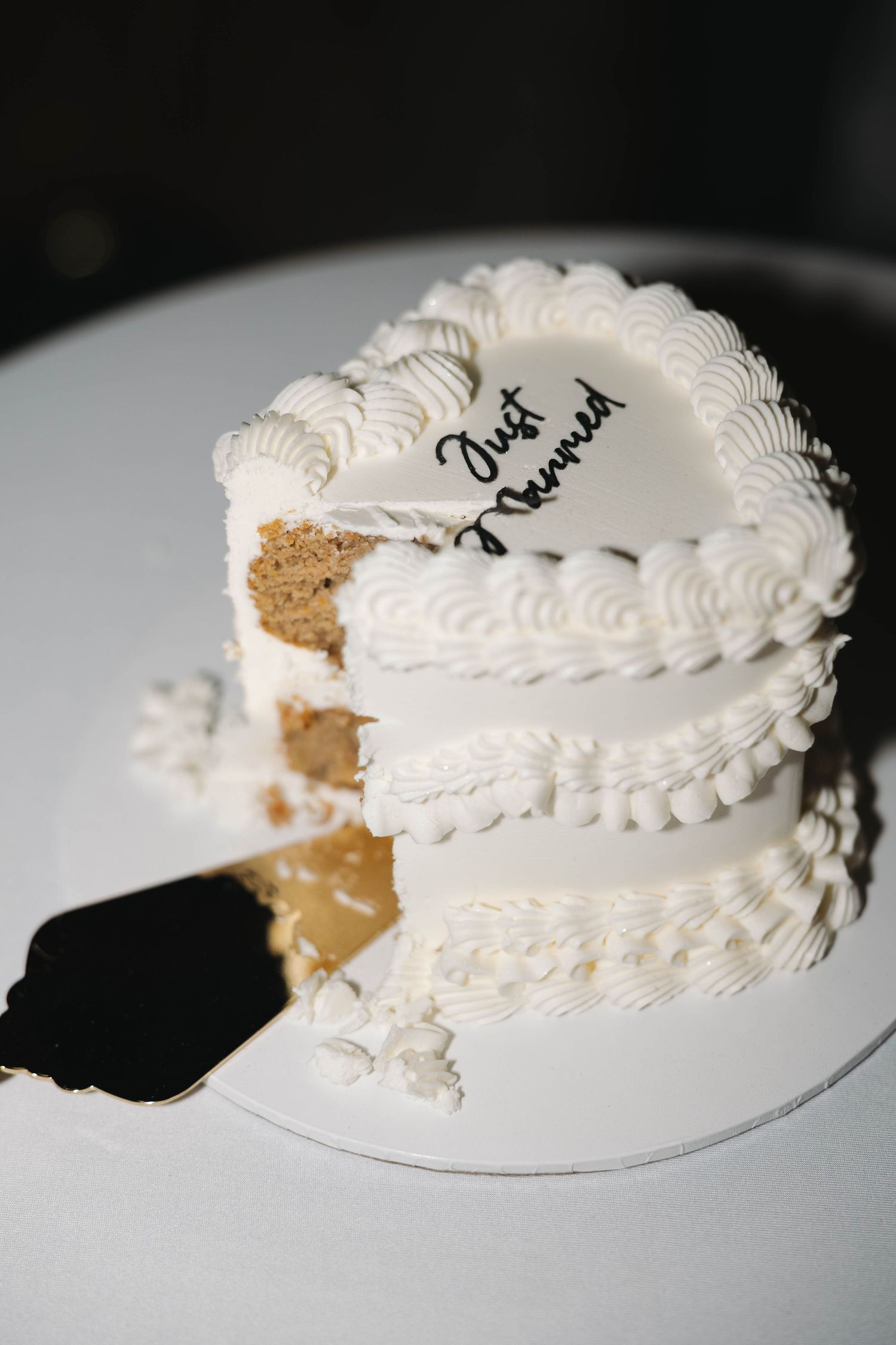 White heart-shaped wedding cake with Just Married inscription and piped frosting details, with a slice removed.