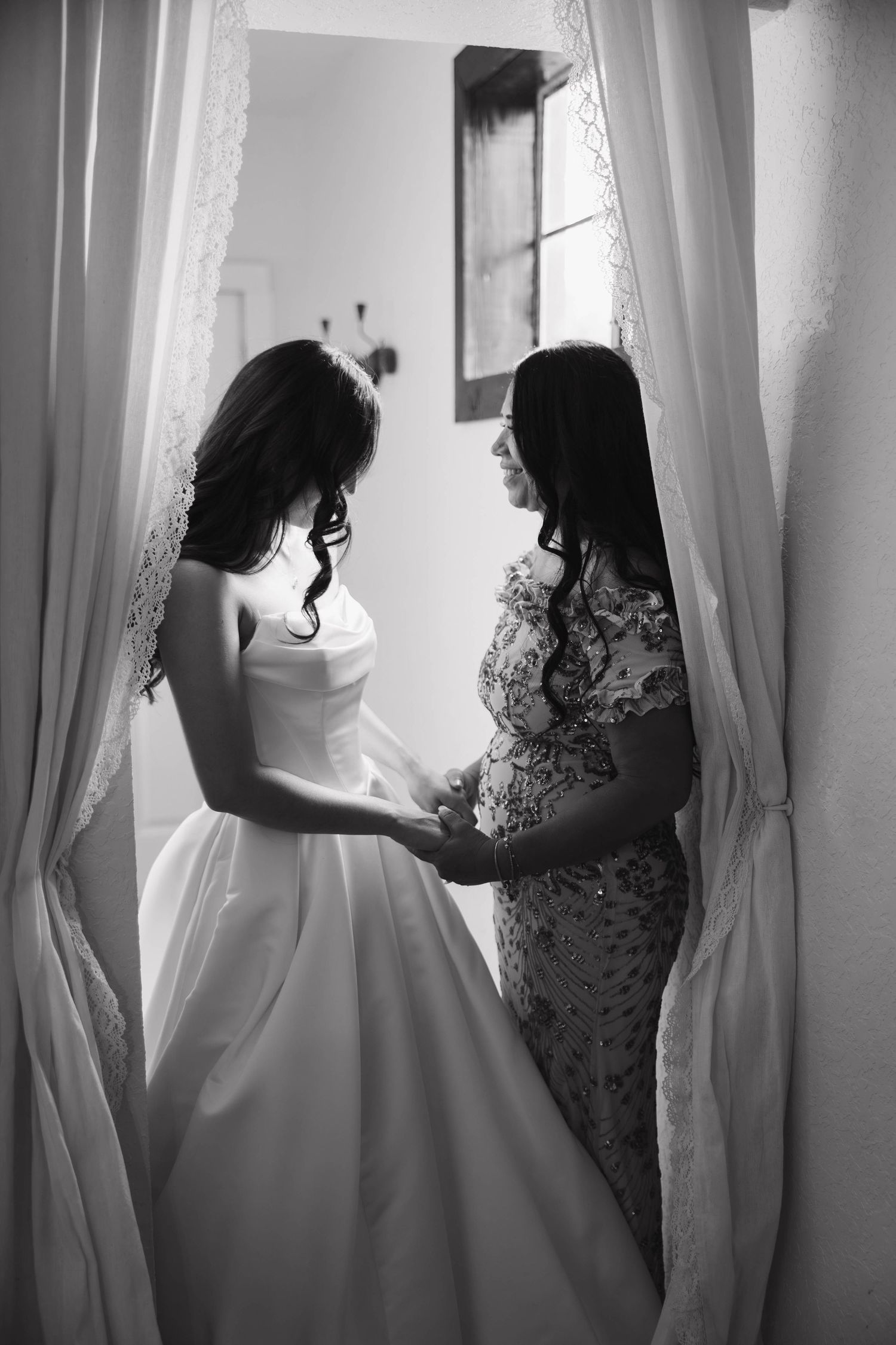 Black and white photo of bride and woman holding hands between curtains.
