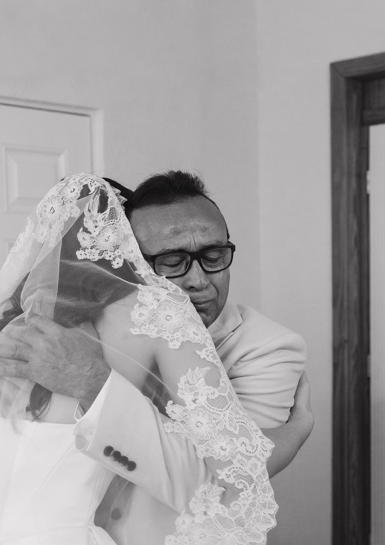 Emotional father embracing his daughter in a wedding veil in a black and white photo.