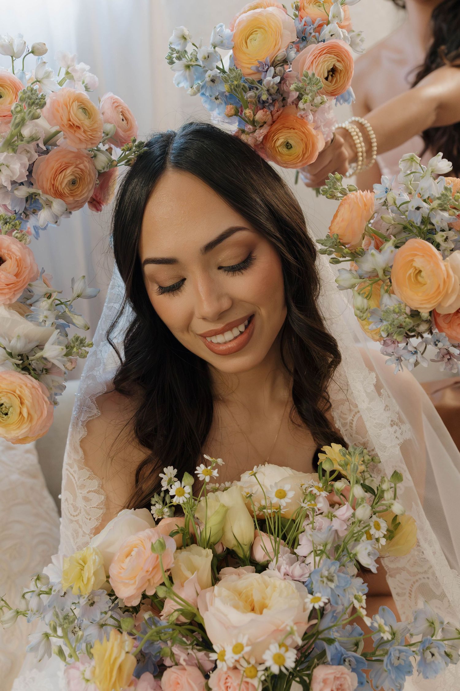 Smiling bride in white strapless gown holds pastel bouquet surrounded by vibrant orange and blue floral arrangements.