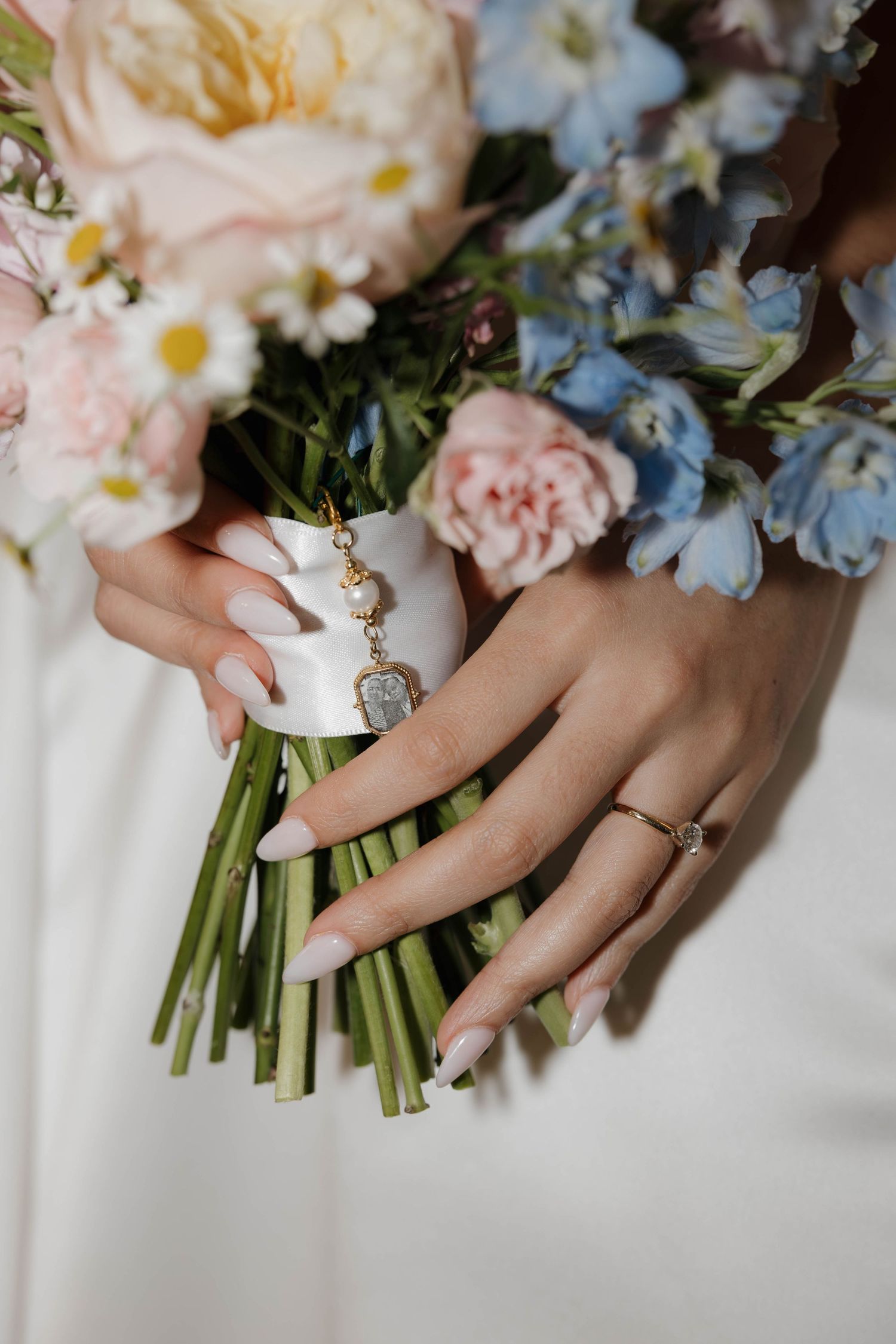 Bride holding pastel floral bouquet with French manicure nails and delicate engagement ring.