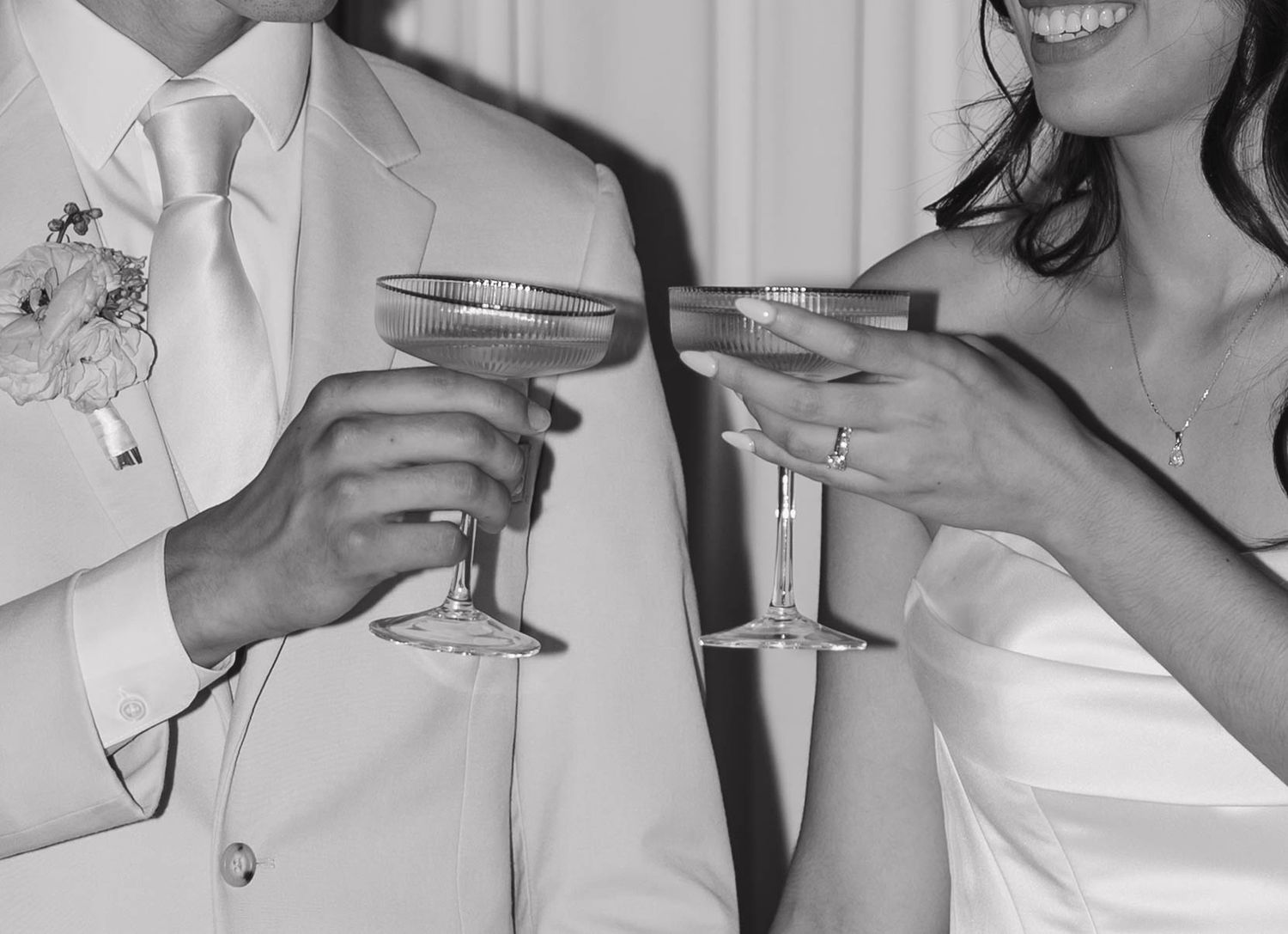 Black and white photo of bride and groom clinking champagne glasses during wedding toast celebration.