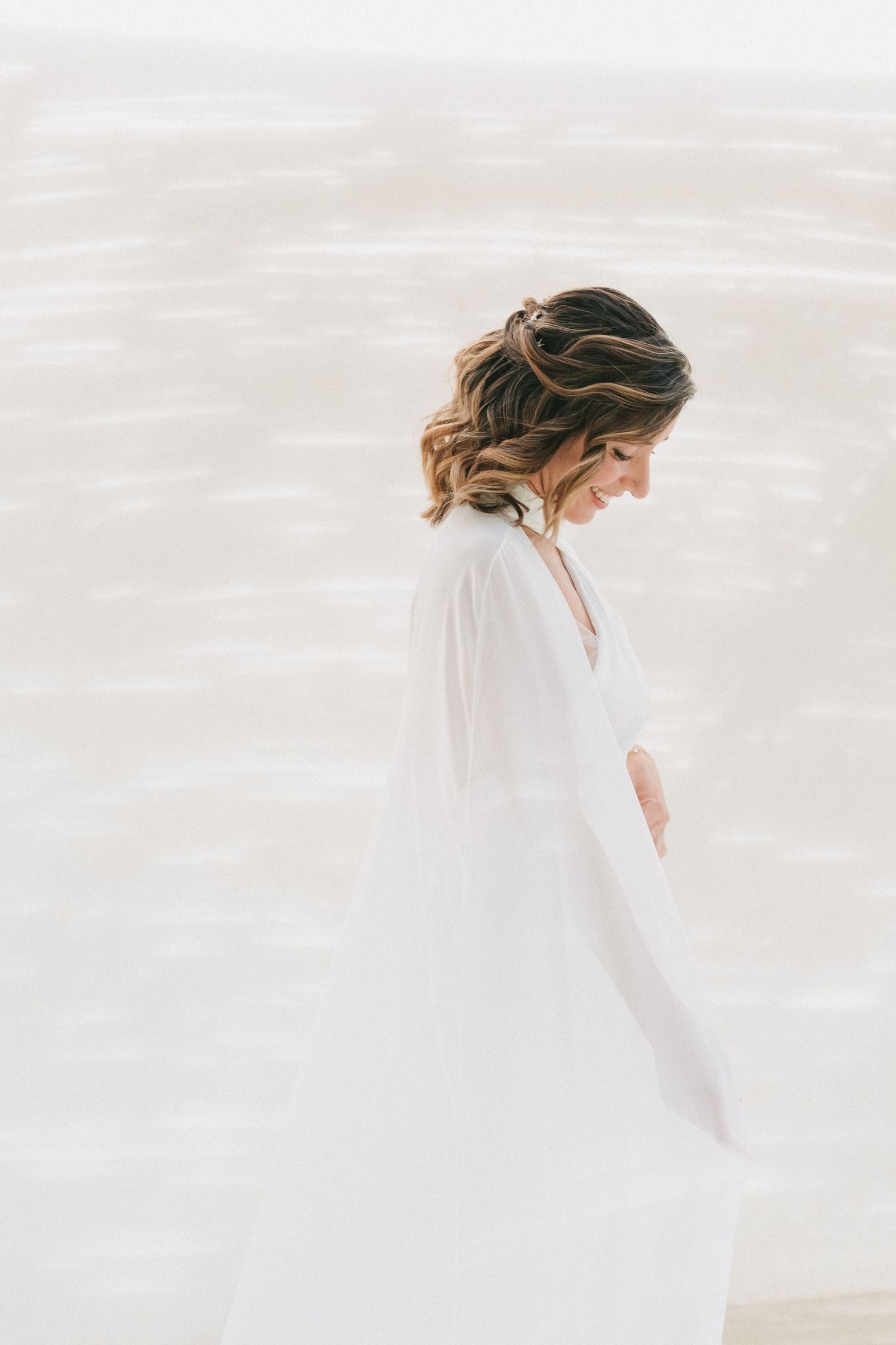 Bride in flowing white dress holding rustic bouquet against neutral background.