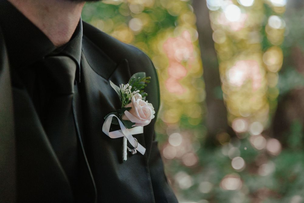 Close-up of a groom's black suit lapel with a pink rose boutonniere tied with a white ribbon bow.