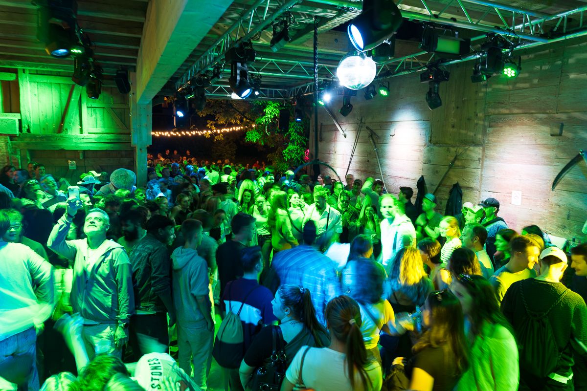 Crowded nightclub dance floor bathed in green neon lights with partygoers dancing in a large venue.