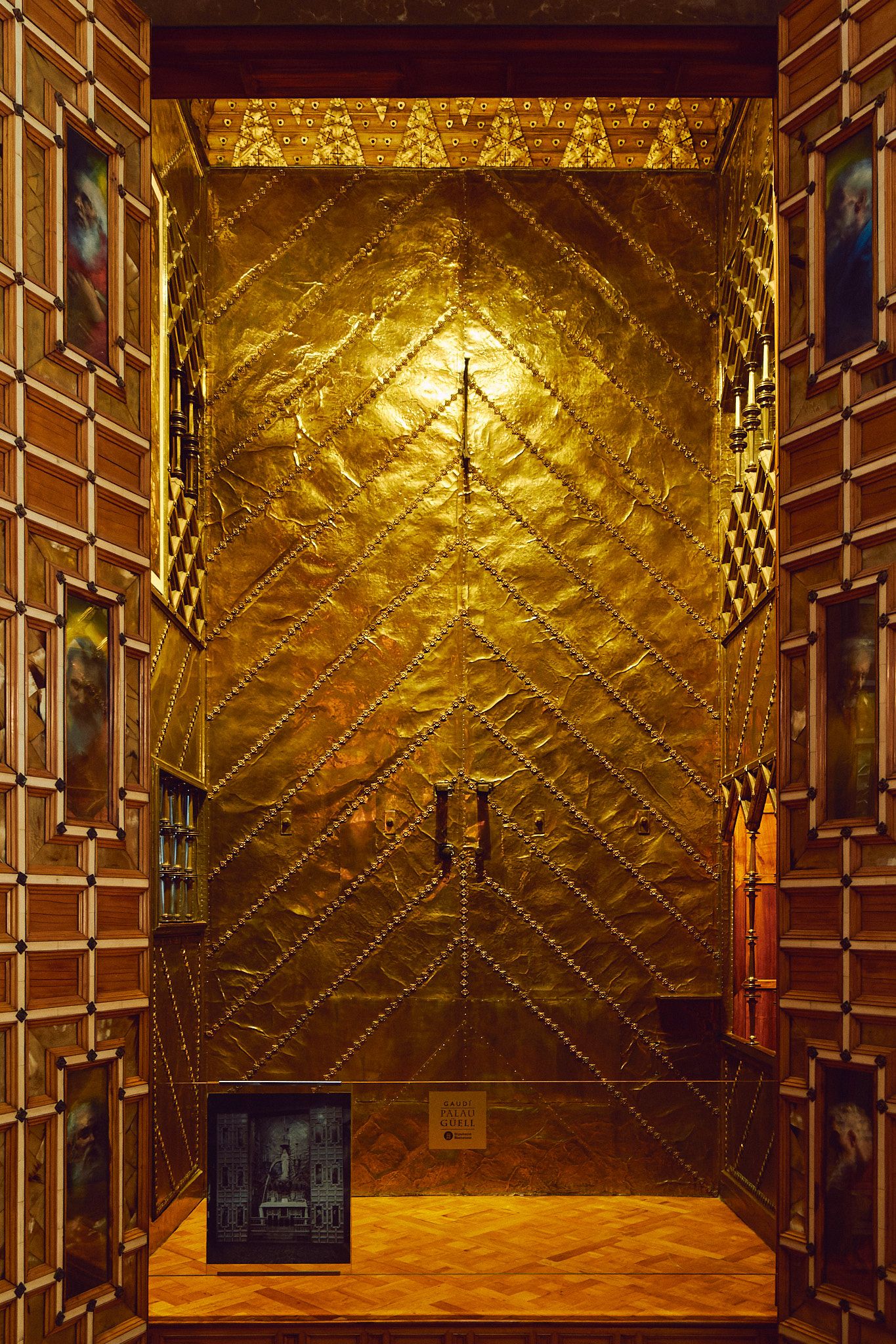 Ornate golden quilted double doors with rivets, framed by wood-paneled walls with artwork in a luxurious interior.
