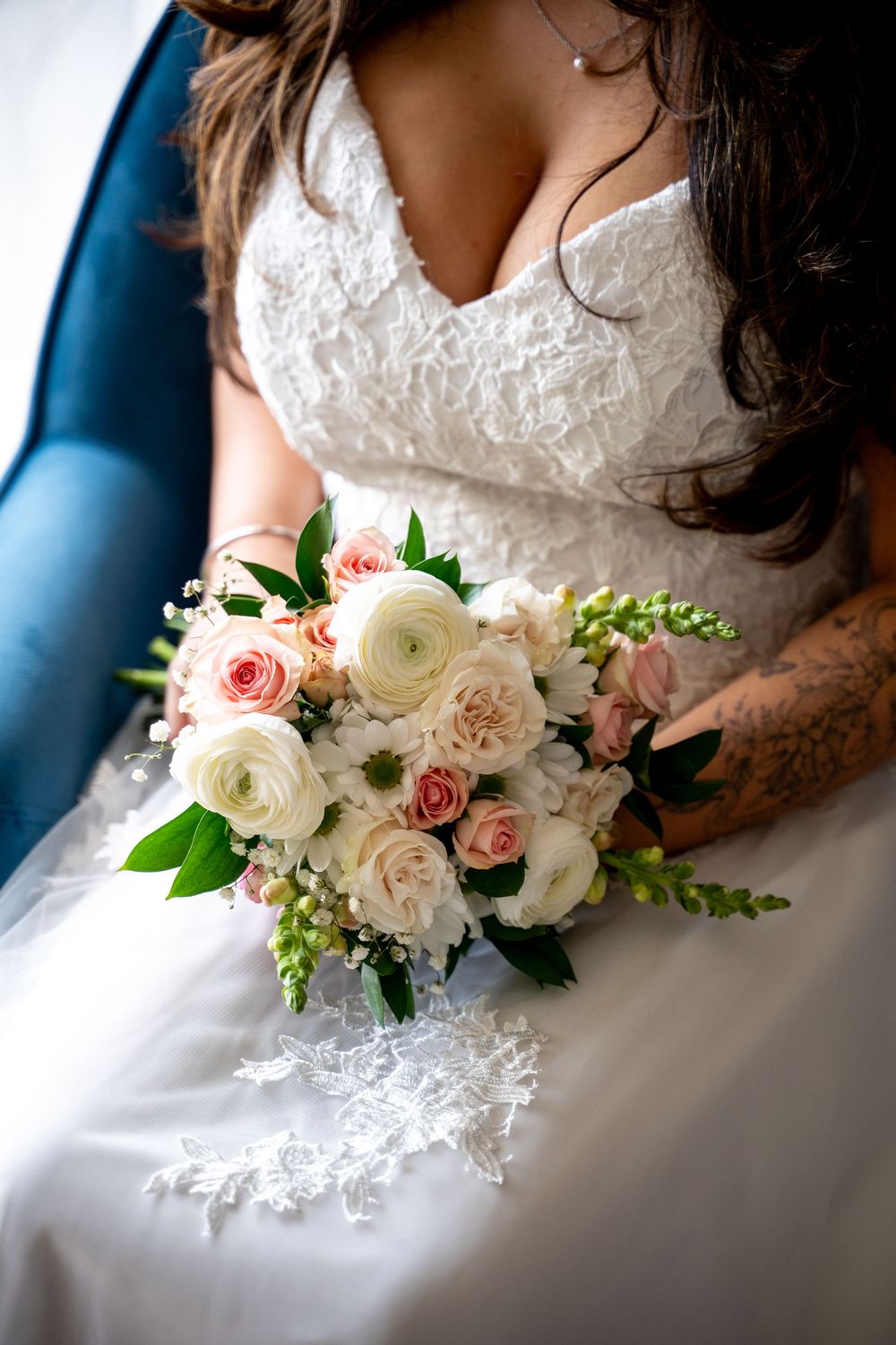 Bride in white lace gown holding elegant bridal bouquet with blush pink roses, white ranunculus, and greenery.