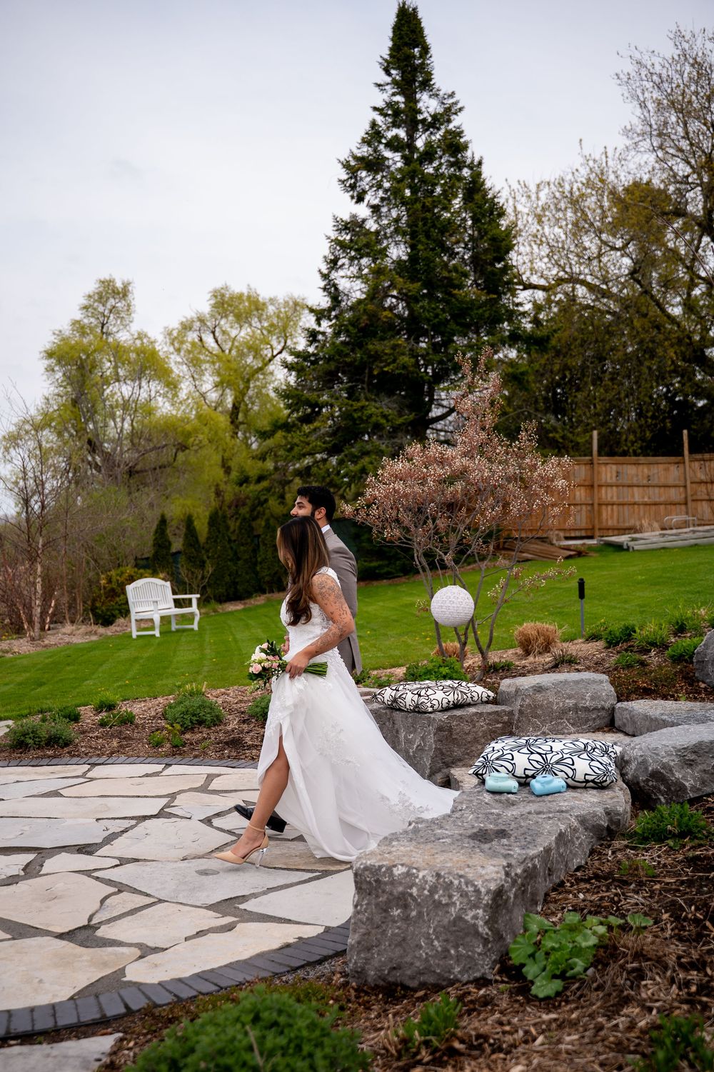 Bride and groom walk through a lush garden on their wedding day, bride in white gown holding bouquet.