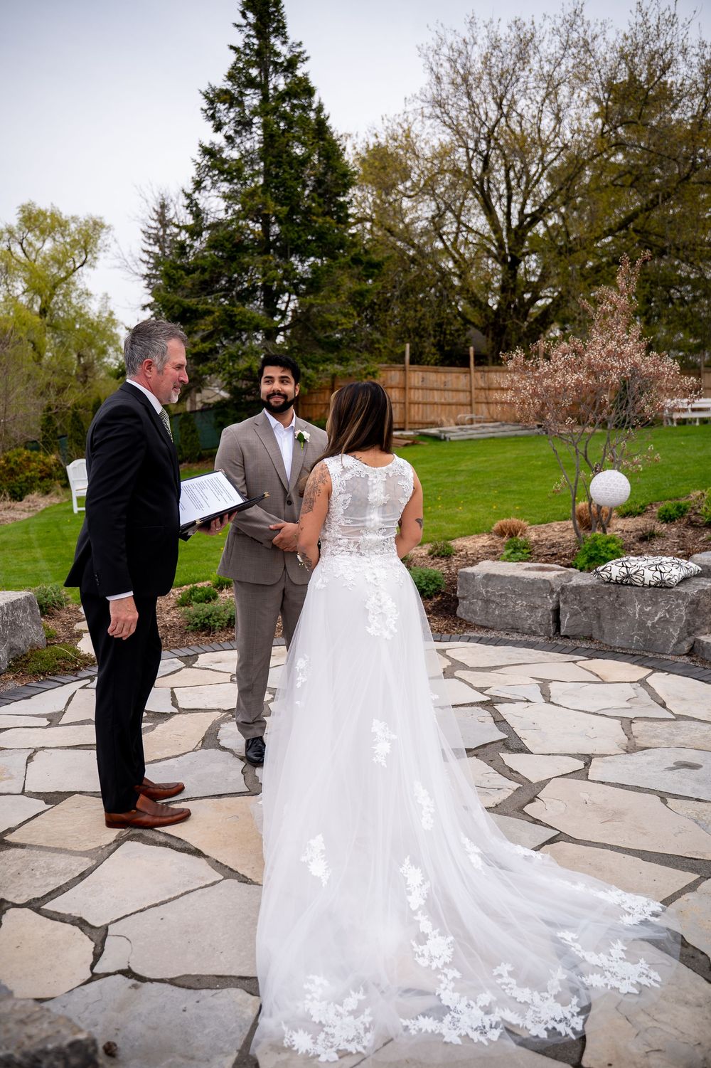 Bride and groom exchange vows on stone patio with officiant during intimate outdoor wedding ceremony.