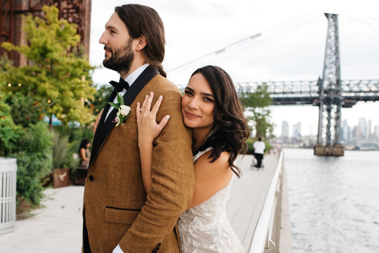 Smiling bride and groom holding a tropical wedding bouquet with pink anthuriums, roses, and bird of paradise flowers.