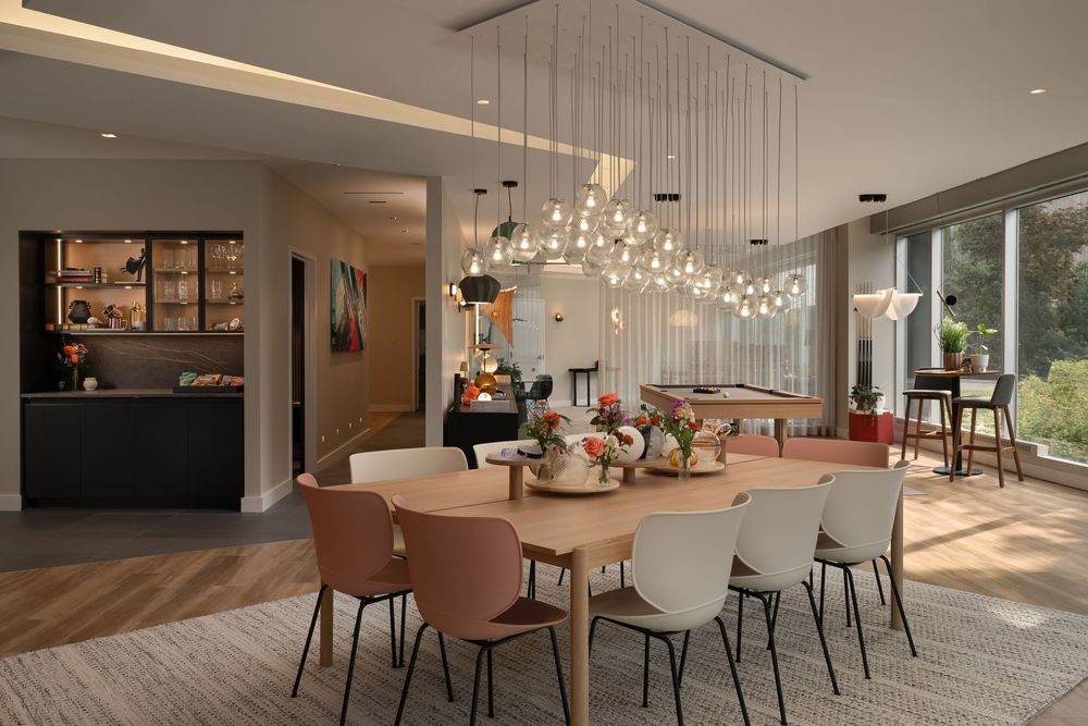 Modern dining room with wooden table, colorful chairs, and elegant pendant lighting fixture above.