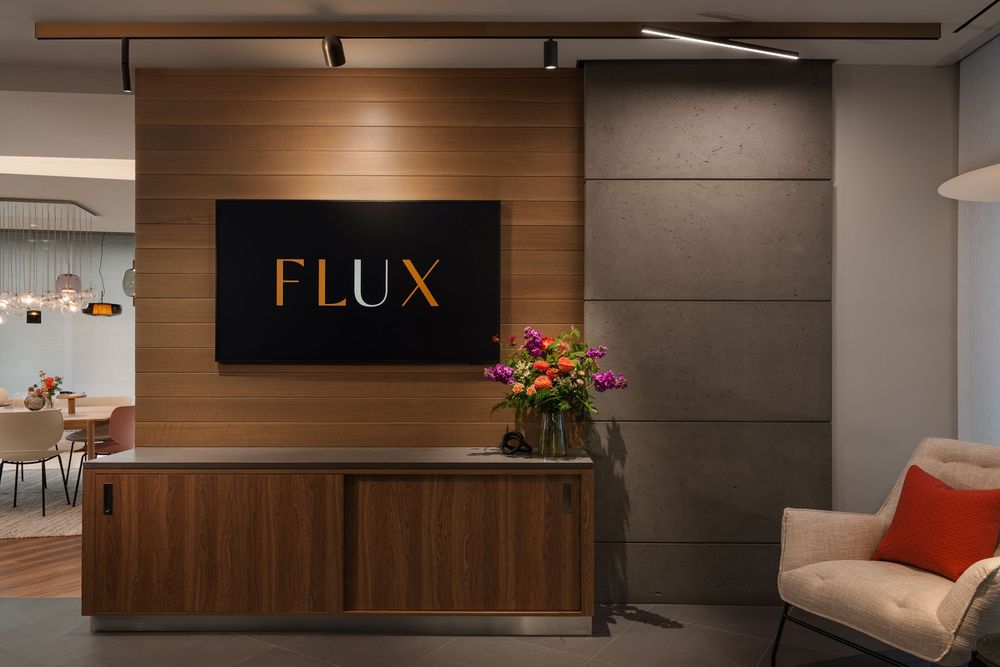 Modern Flux office reception desk with wood paneling, TV logo display, fresh flowers, and stylish seating area.