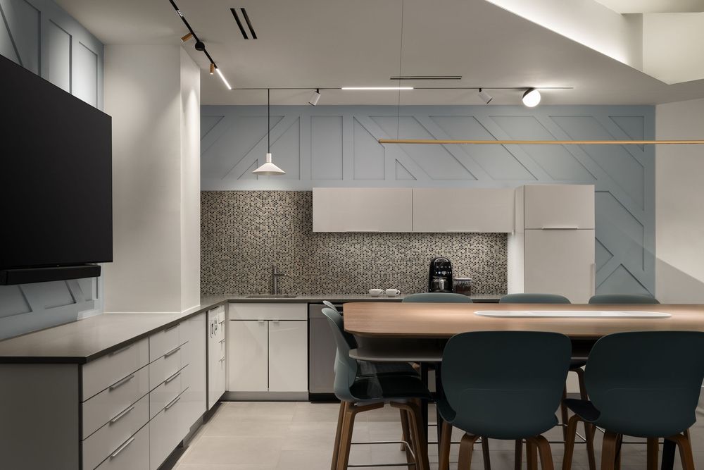 Modern kitchen with blue geometric accent wall, white cabinets, stainless appliances, and dining table with teal chairs.