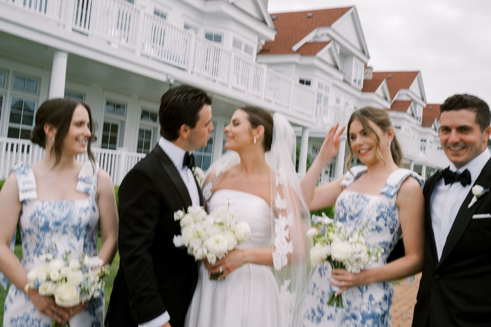Wedding party poses outside elegant venue, bride in white gown with veil, bridesmaids in blue floral dresses, groomsmen in tuxedos.