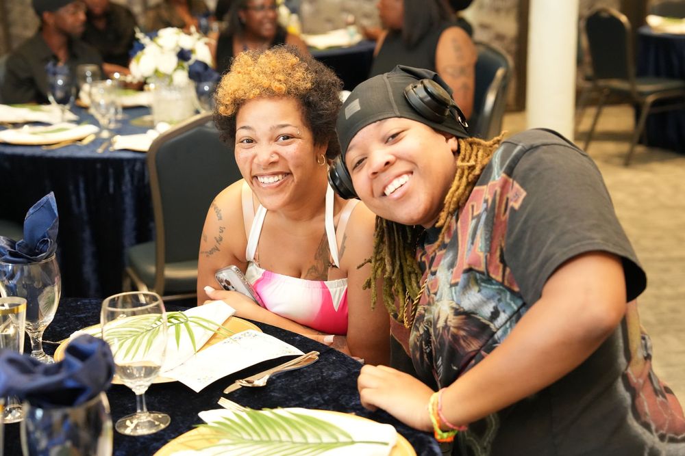 Two women smiling and posing together at a banquet table with elegant place settings and decorations.