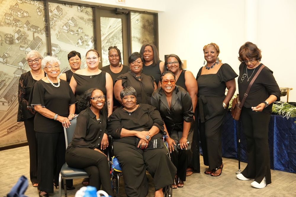 Group of elegantly dressed women in black attire posing together at a formal event or gala celebration.