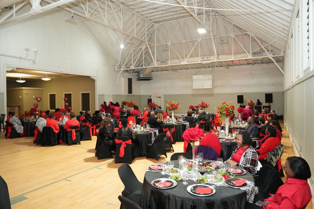 Elegant banquet hall with round tables draped in black and red linens, filled with guests at a formal dinner event.