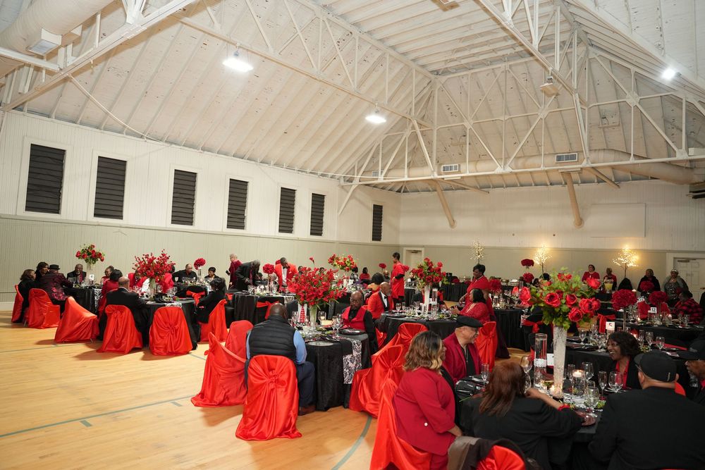 Elegant banquet hall decorated in red and black with floral centerpieces and guests seated at round tables.