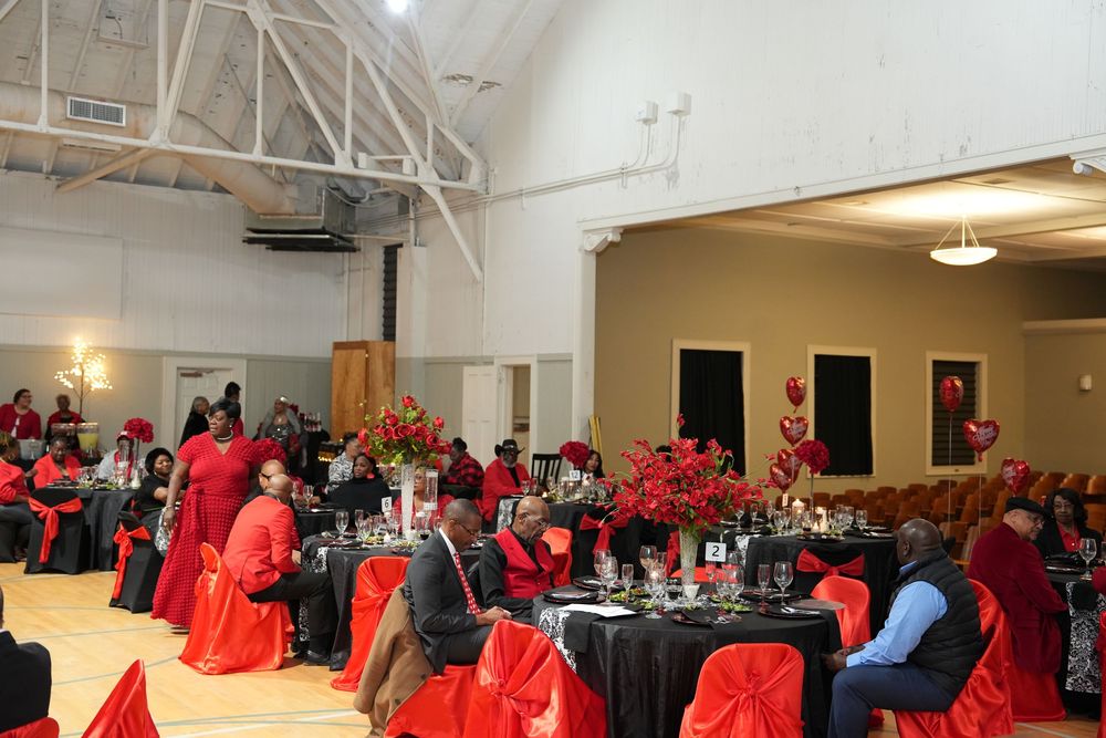 Elegant Valentine's Day banquet hall with red and black decor, floral centerpieces, and guests seated at decorated tables.