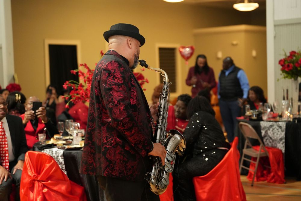 Saxophonist in red floral jacket performs at elegant Valentine's Day banquet with red decorations and seated guests.