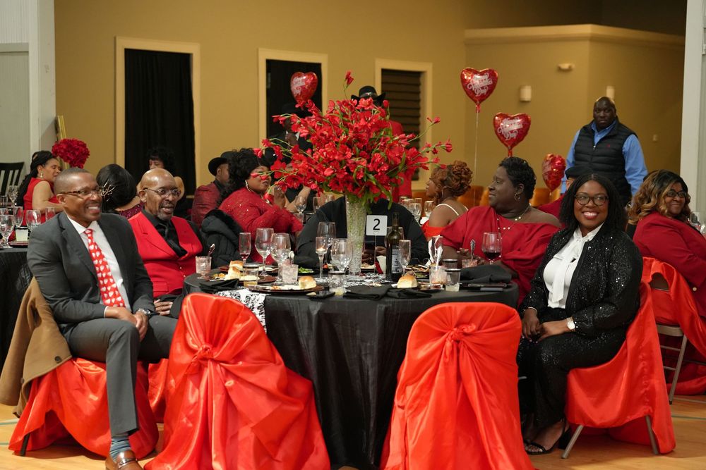 Guests in red and black attire seated at elegantly decorated banquet tables with red floral centerpieces at a formal event.
