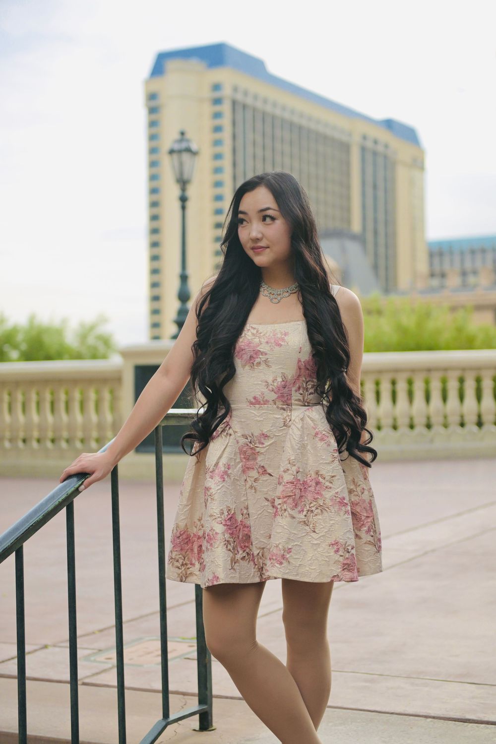 Young woman in floral dress posing by railing with Las Vegas hotel in background.