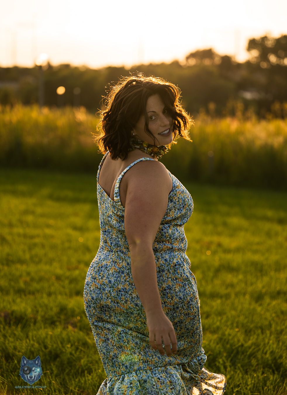 Woman in blue floral sundress glances back smiling during golden hour sunset outdoors. Chi.Shooters meet gabbsbosh