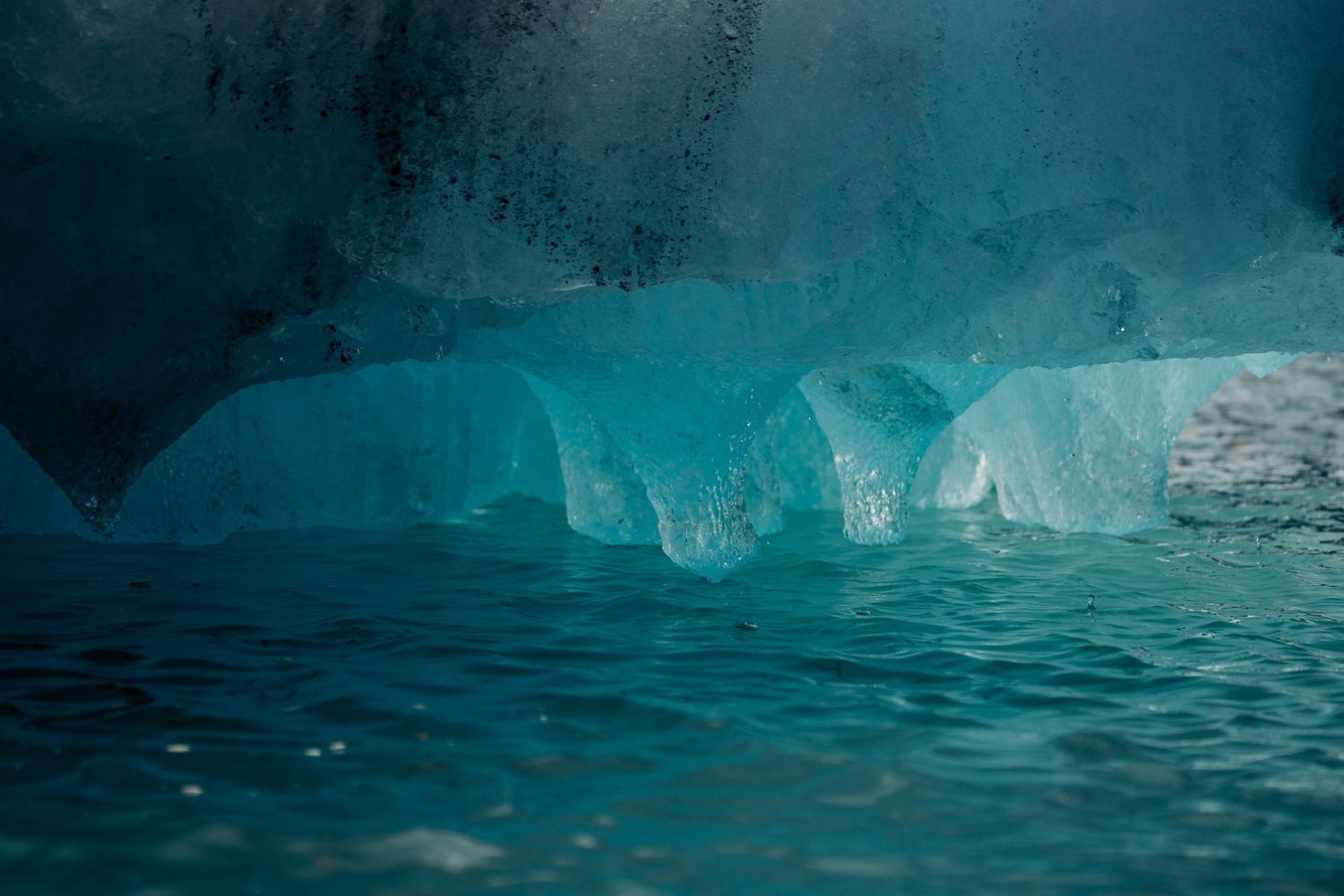 Base turquoise lumineuse d'un iceberg sous son surplomb sombre, clapot au premier plan