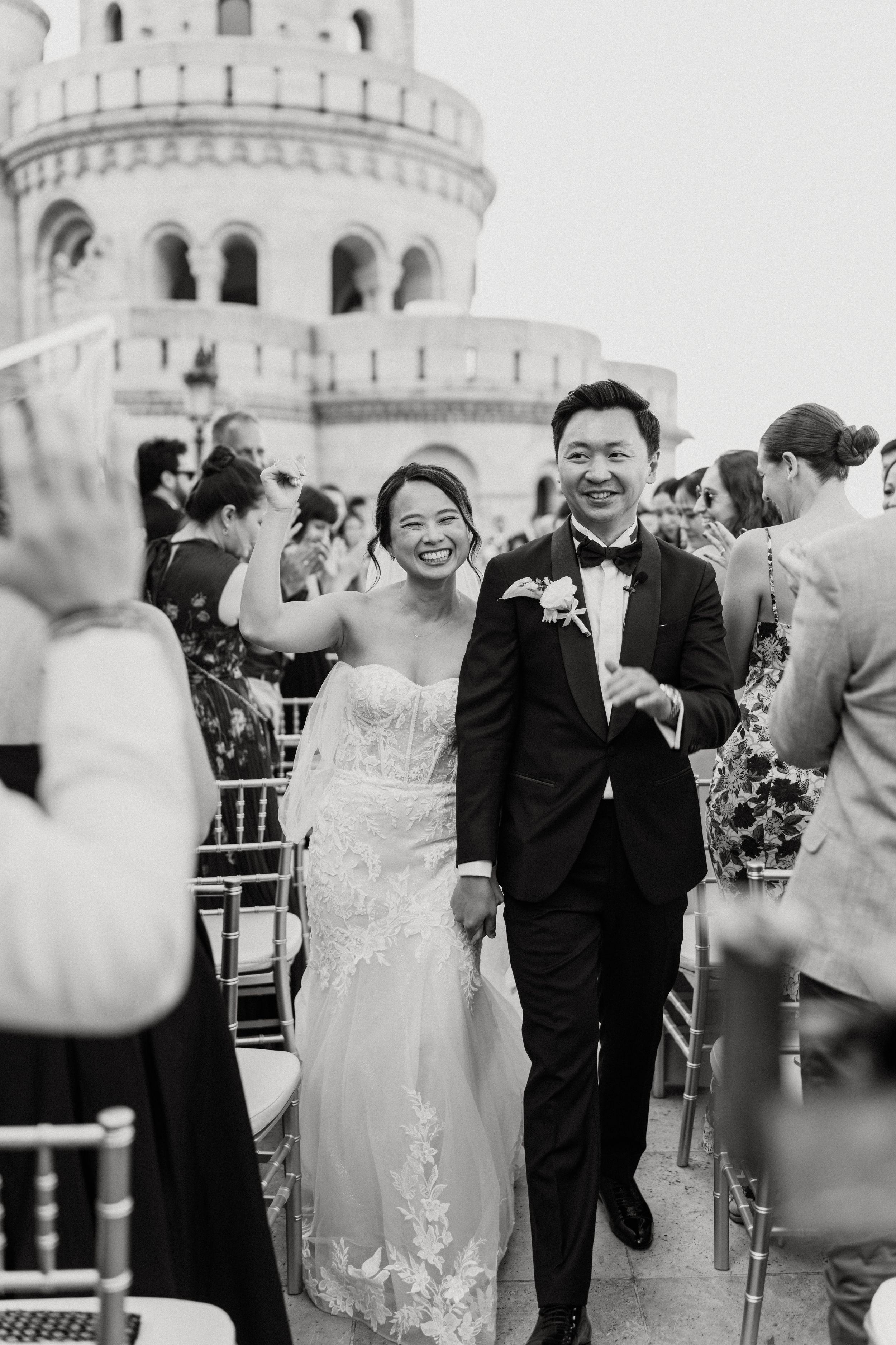 Black and white photo of smiling newlyweds walking down aisle at Fisherman's Bastion Budapest wedding.
