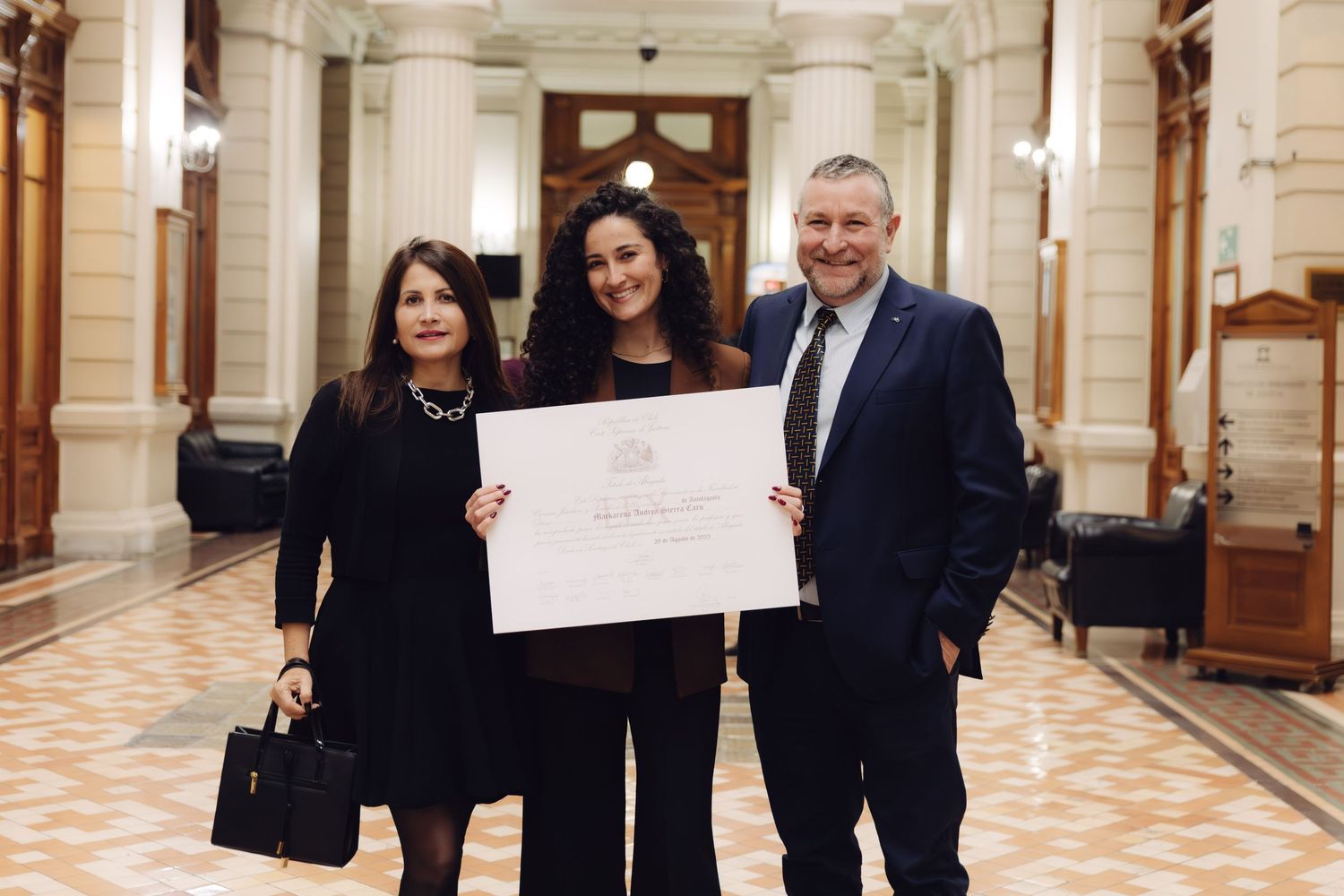 Three people pose with a certificate in an elegant hallway.