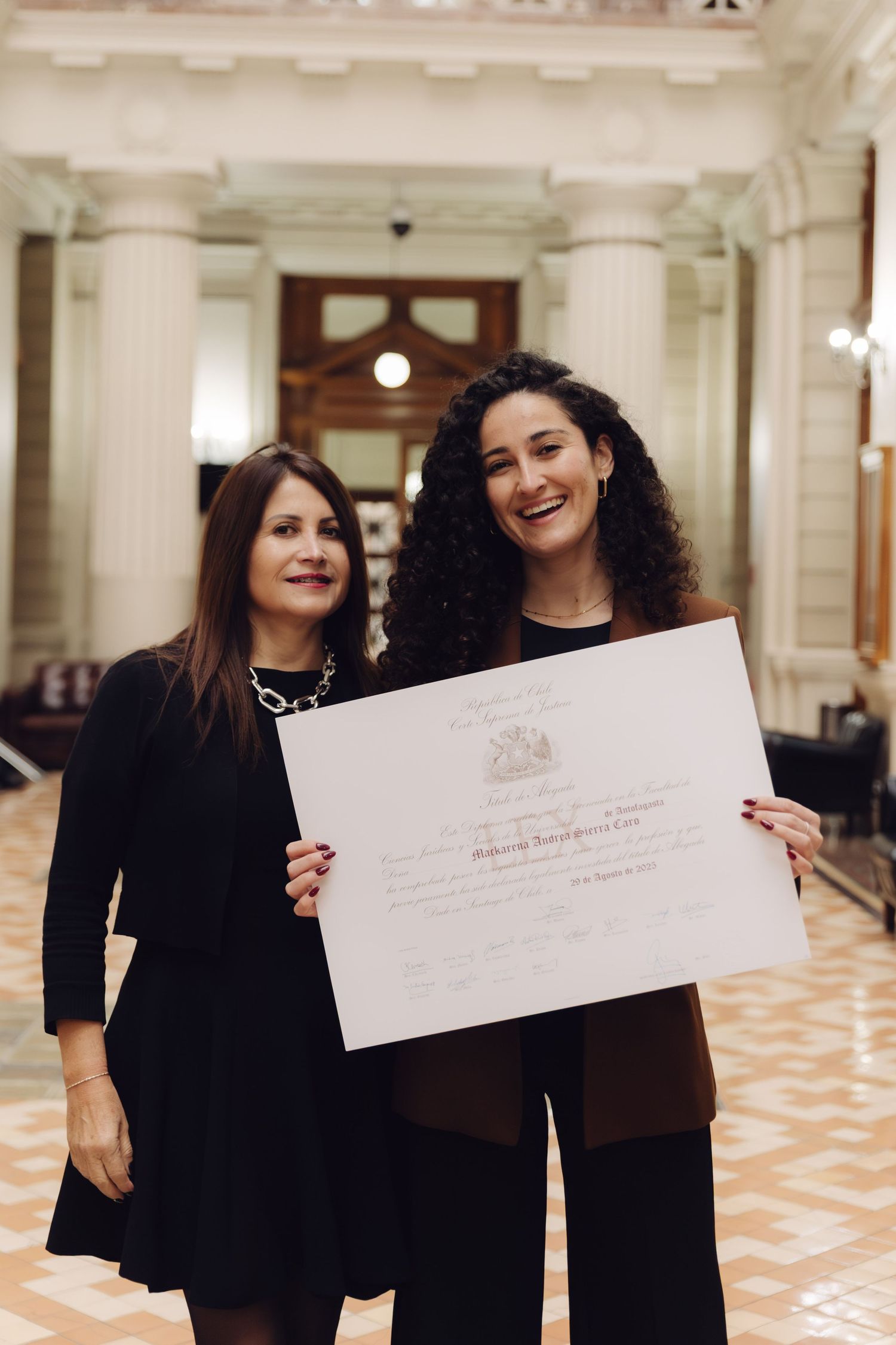 Two women pose together holding a large official certificate.
