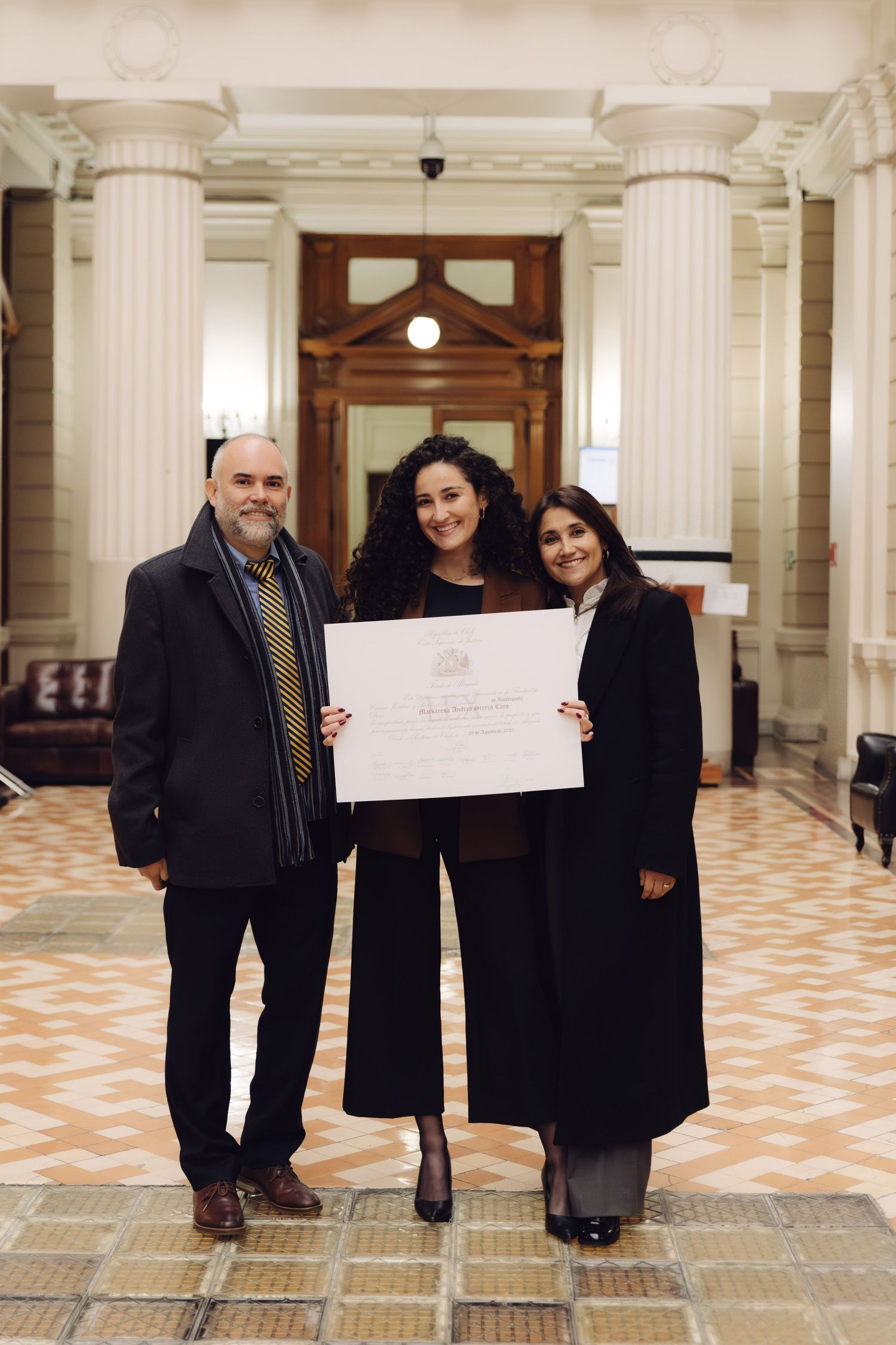 Three people pose with a certificate in a columned building.