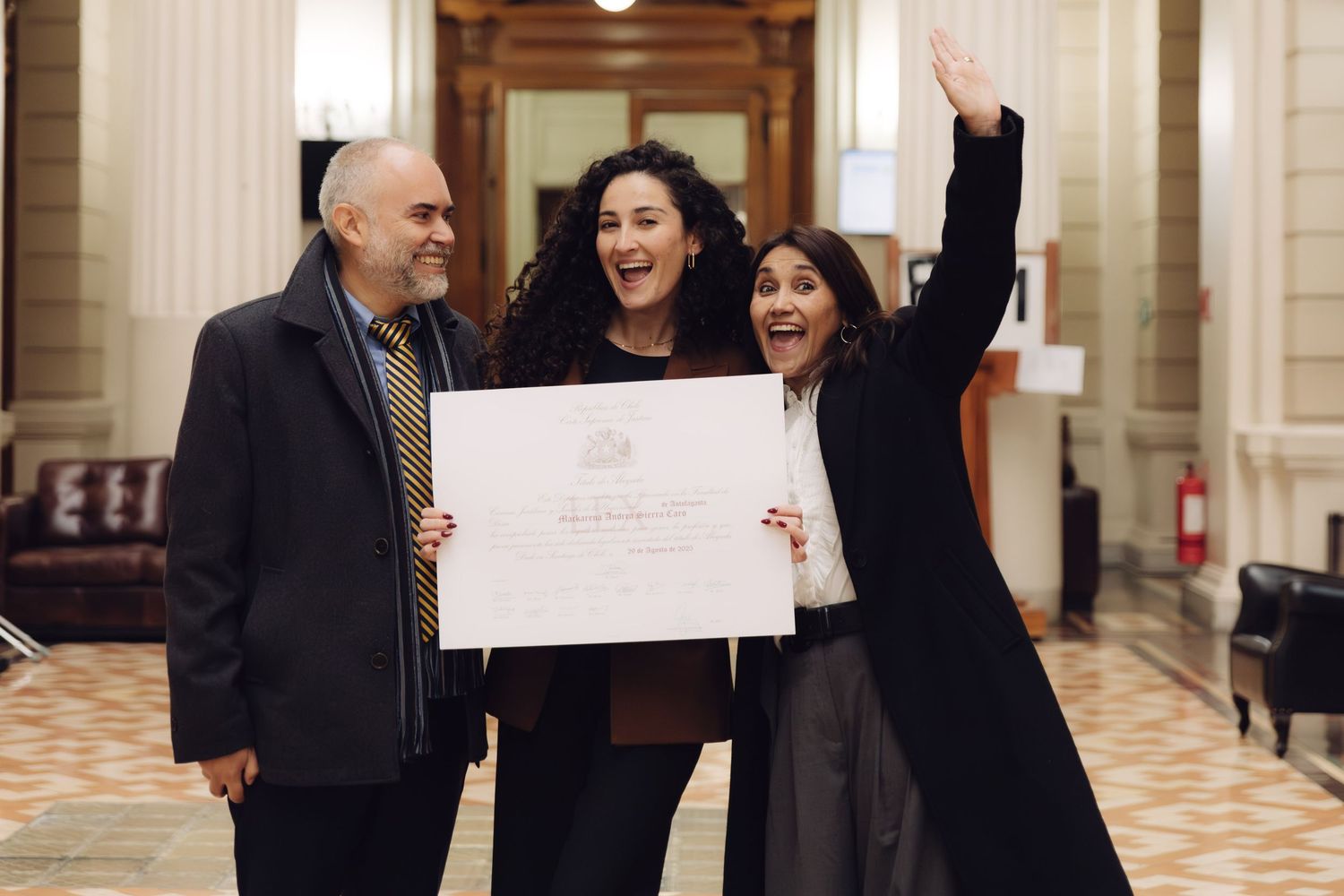 Three people celebrate joyfully with a certificate indoors.